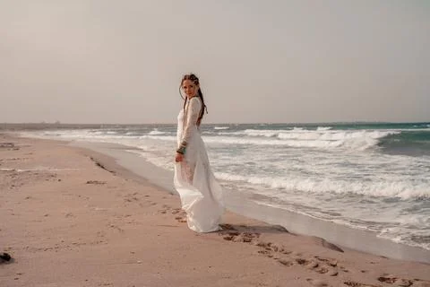 Model in boho style in a white long dress and silver jewelry on the beach. Her Stock Photos