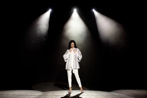 Model demonstrates clothes on the stage in the rays of white light, dark Stock Photos