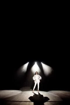 Model demonstrates clothes on the stage in the rays of white light, dark Stock Photos