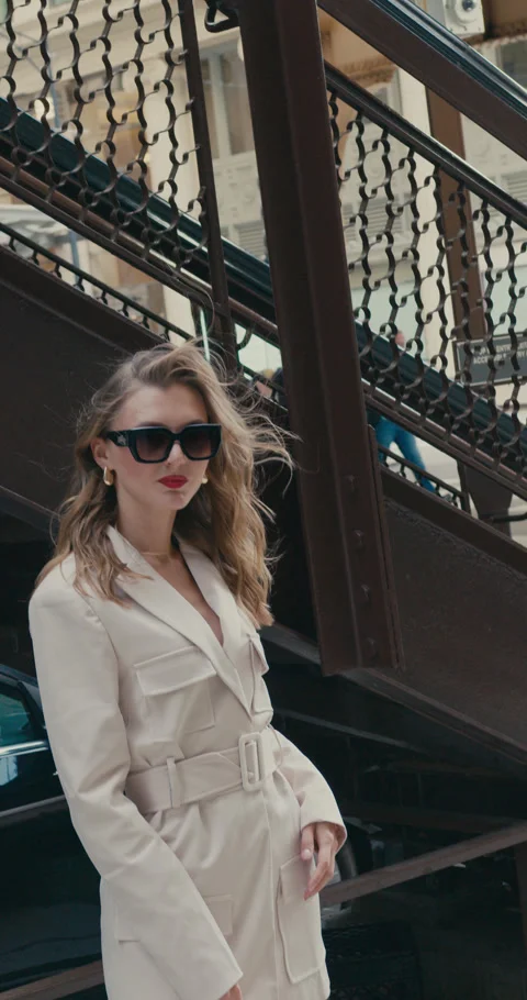 Model dressed in cream blazer stands confidently on metal stairs with elegant Video stock 322719824