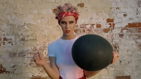 Model eats big black balloon against a brick wall Stock Footage 67657983