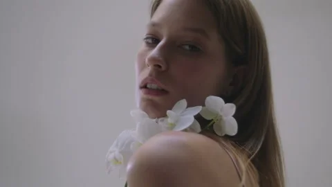 Model elegantly posing with a white orchid in a soft setting Vídeos de archivo 319925468