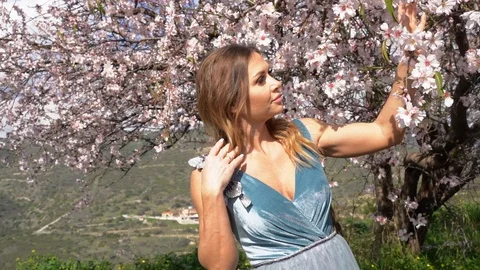 Model in a fancy dress posing with a blooming almond tree Video stock 125763647