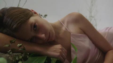 Model gazing into the camera surrounded by lush greenery in soft light Stock Footage 319924693