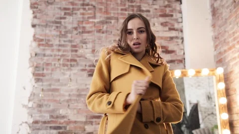 Model Girl in orange coat posing at home in the mirror and brick wall, slow mo Stock Footage 105008399