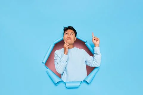 Model guy posing thoughtfully inside the cut in blue background, wearing white Stock-Fotos