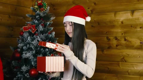 The model is holding a striped gift box near a decorated Christmas tree Stock Footage 319825633