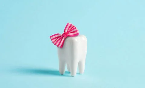 Model of human tooth with pink bow on blue background. Minimal cute postcar.. Stock Photos