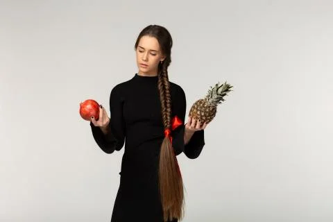 Model with long braid and red bow in black dress can not choose what eat first Stock Photos