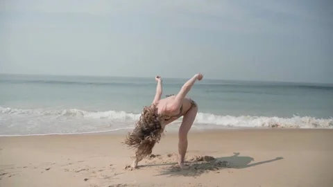 A model-looking girl is dancing on a sandy beach, the sea is blue behind her. Video stock 228823791