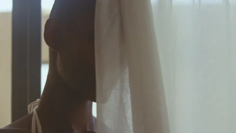 Model looking straight at camera from behind white curtains Stock Footage 275690087