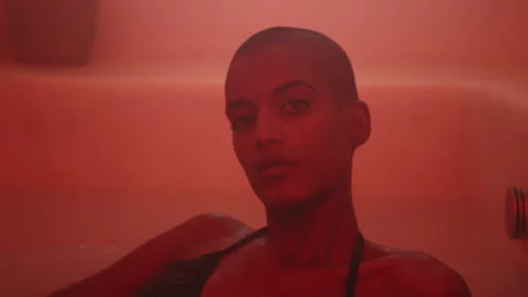 Model lying in bath with swimsuit looking straight at camera in red light Stock Footage 275353004