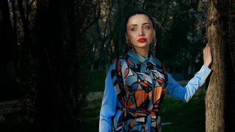Model with makeup in handmade earrings stands at tree trunk Stock Footage 108261276