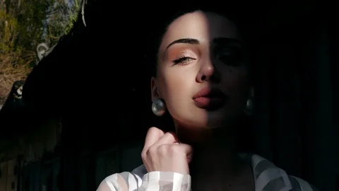 Model with makeup in silver earrings stands in partial shade Stock Footage 108260332