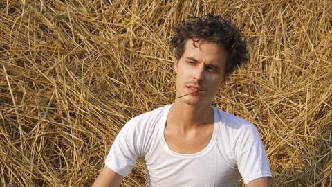 Model man with a straw in mouth on a haystack background Foto stock