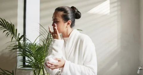 Model opening jar, dipping fingers and massaging face upward by blinds and plant Stock Footage 344104717