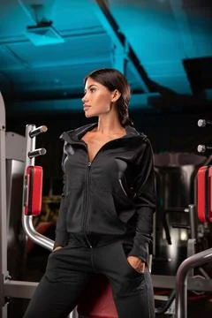 Model poses confidently in sleek black activewear against backdrop of modern gym Stock Photos