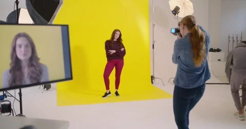 Model posing on yellow backdrop, photog signaling, framing cam, crew moving 스톡 동영상 347450140
