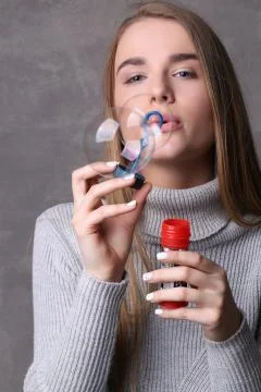 Model in pullover blowing bubbles. Close up. Gray background Stock Photos
