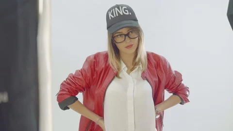 Model in red coat and balck baseball hat wearing glasses poses during photo Stock Footage 99688259