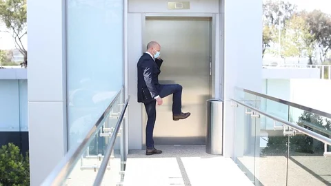 A model released mask wearing man kicks an elevator button during the Covid-19 Stock Footage 128970390