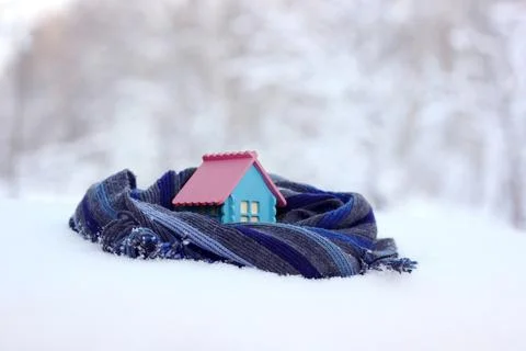 A model of a rustic house wrapped in a warm scarf on a blurry winter backgrou Stock Photos