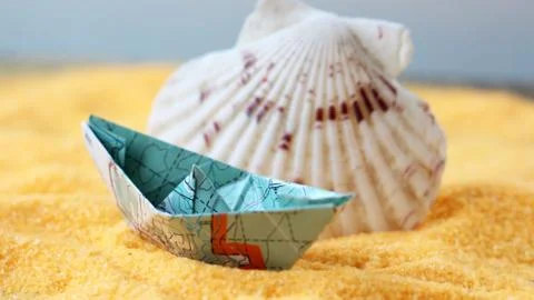 Model of a ship from a paper map on the sand and a seashell Stock Photos