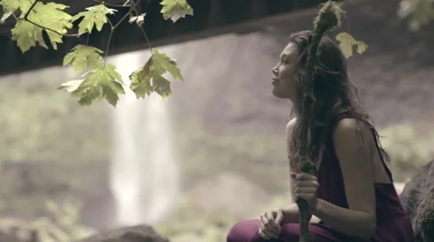 Model Sits Beneath Tree, Looks Around, Beautiful Waterfall In Background Vidéo 56064625