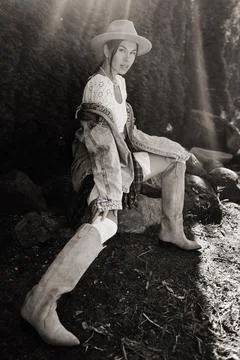A model sits elegantly on a rocky surface, showcasing trendy cowboy boots and Stock Photos
