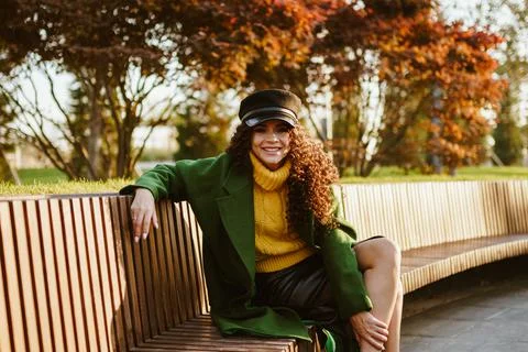 Model sits on a park bench throwing her foot on her leg and smiling Stock Photos