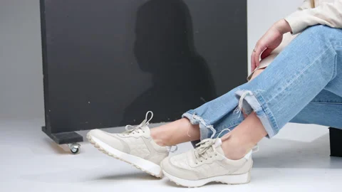 Model sitting on a step and touching her white sport shoes laces. Video stock 235401700