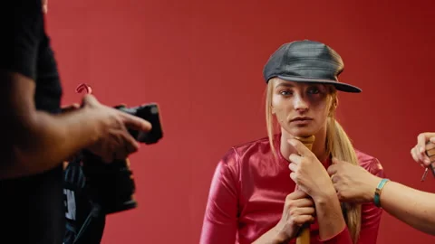 Model sitting while makeup artist works on her in front of red background Video stock 275342757