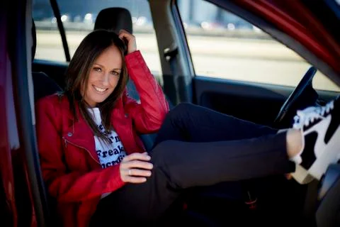 Model smiling inside a car with a red jacket and sneakers Stock Photos