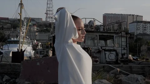 Model stands sideways against abandoned structures and yacht Stock Footage 117887527