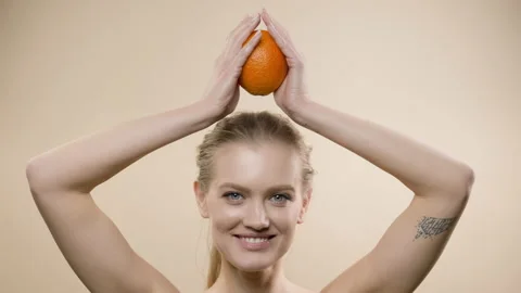 Model In Studio Posing. Young Blonde With Long Hair Holding An Orange. She Holds 스톡 동영상 152853655