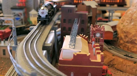 Model toy trains turn a corner around a mountain and a small town city Stock Footage 52551174