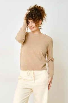Model wearing a light brown sweater and cream pants posing against a plain .. Foto stock