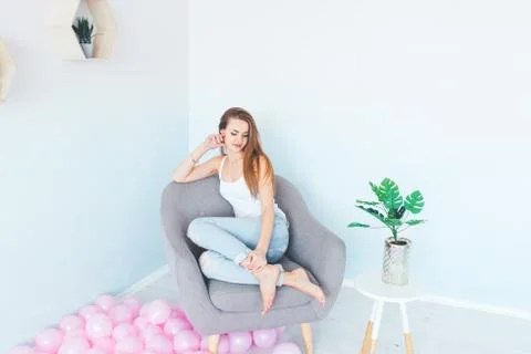 Model in white singlet and blue denim with holes sitting into the grey armchair. Stock Photos