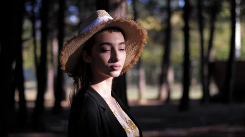 Model in yellow straw hat lit by sun stands in dense forest Stock Footage 121063745