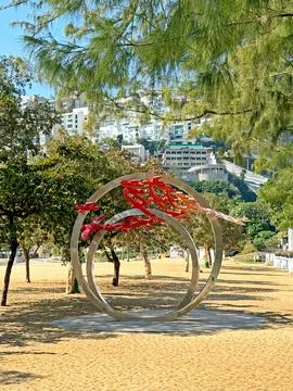 Modern abstract sculpture with red elements on a sandy beach with buildings.. 스톡 사진