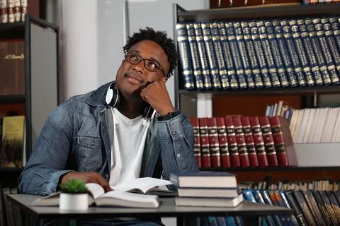 Modern African student prepares classes in office with books dreamily looking up Foto stock