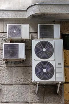 Modern air conditioner climate system devices hanging outside on building facade Stock Photos