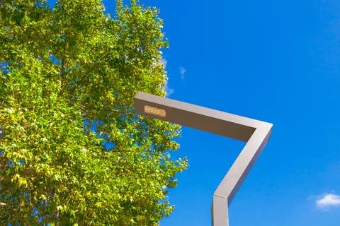 Modern angular street lamp with LED light against bright blue sky and green.. Stock Photos