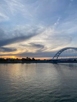 Modern arch bridge spanning river at sunset, sun illuminating water Stock Photos