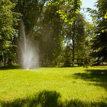 Modern automatic lawn irrigation device in the park. Water is sprayed over la Stock Photos