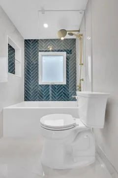 Modern bathroom featuring blue herringbone tile, white fixtures, and gold s.. Stock-Fotos