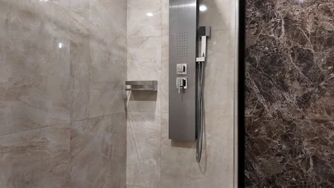 Modern bathroom shower interior with beige marble walls, dark stone accent Stock Footage 345412641