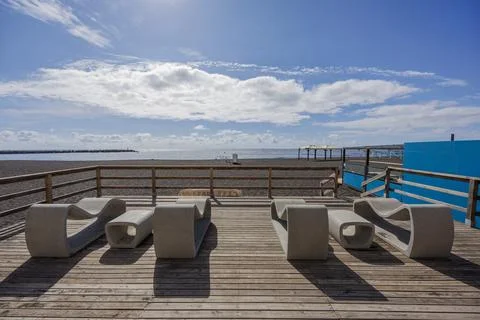 Modern beach deck with empty benches and calm sea under bright sky Stock Photos