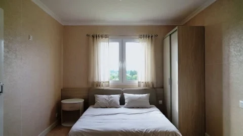 Modern bedroom interior featuring a double bed, wooden furniture, and a window 스톡 동영상 335786236