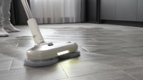 Modern beige vacuum cleaner operating on grey tile floor surfaces Stock Footage 345023855